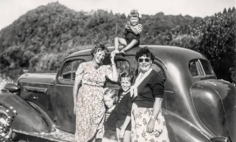A black and white photo of two women and three children with an old Buick.