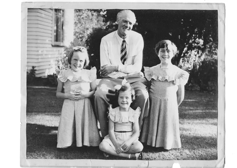 A black and white photo of a man wearing a tie and three girls gathered around him.
