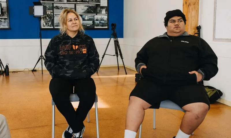 Huia O’Sullivan and a young man sit on chairs during a Ngā Rangatahi Toa workshop, with cameras and lighting equipment behind them.