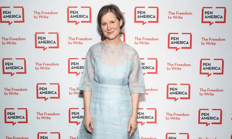A woman in a light blue dress standing against a background with the repeated logo of PEN America.