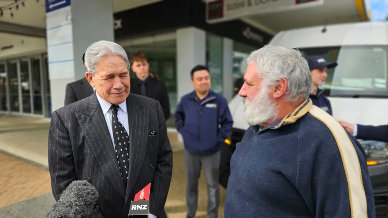 Winston Peters, a grey-haired NZ politician in a dark suit, interacts with a grey-bearded man on Hurstmere Rd in Takapuna.