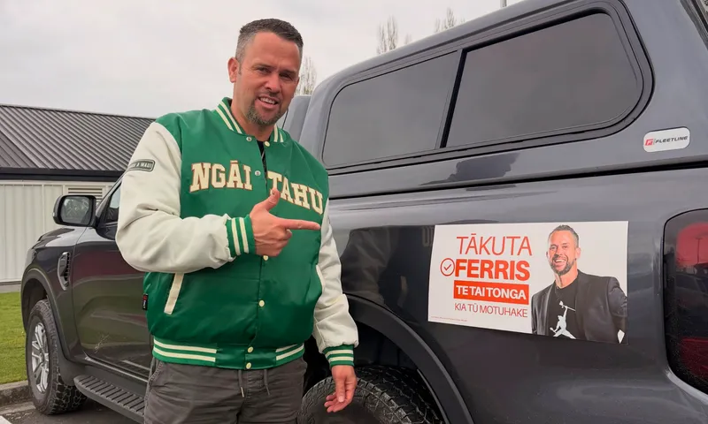 Te Tai Tonga MP Tākuta Ferris points to an election campaign sign bearing his name attached to the side of a ute.
