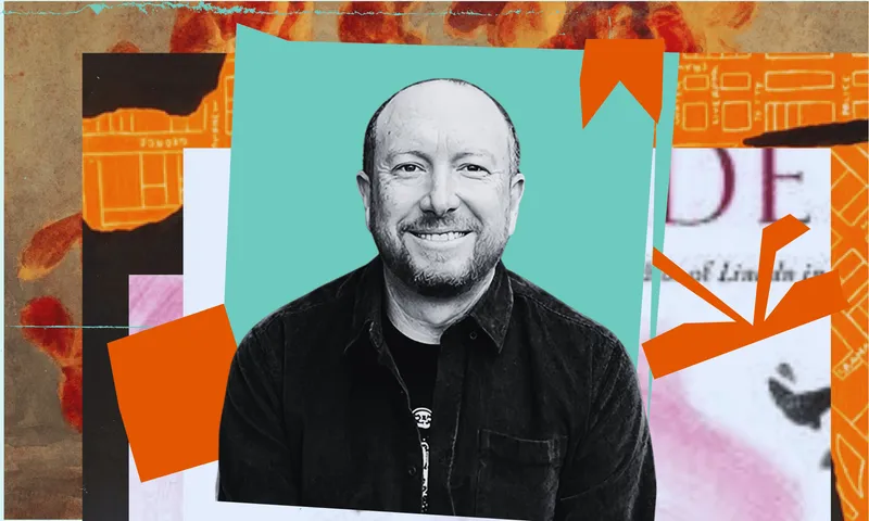 A black and white photo of writer Craig Cliff who is a middle aged man. Behind him is a collage of colours and shapes. He is smiling.