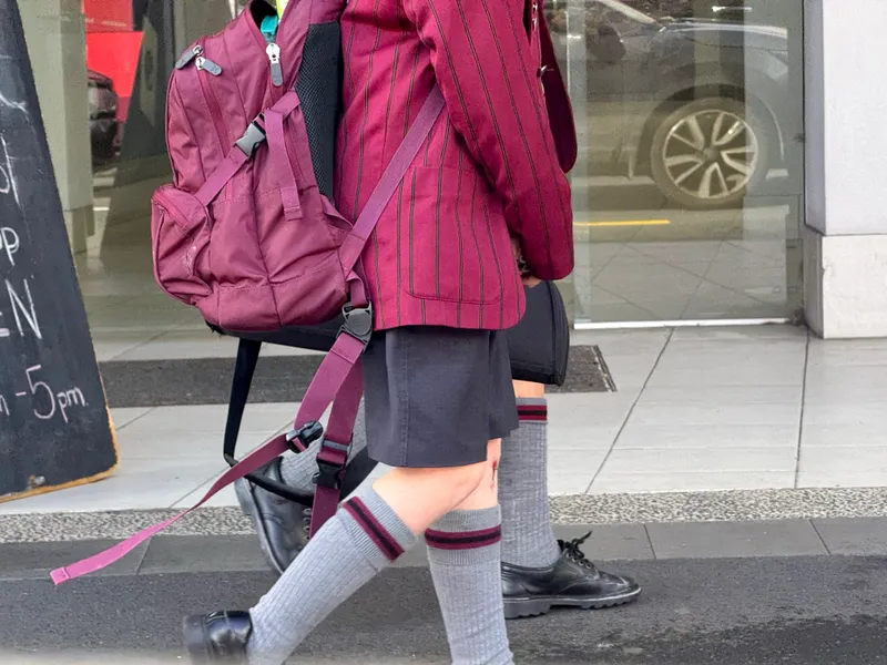 Faceless children in school uniform walk past the camera.