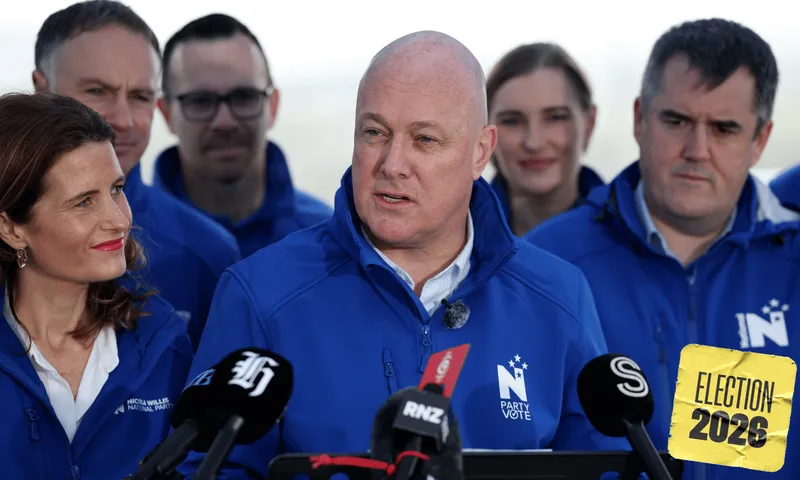 A group of people wearing matching blue jackets with the "N" National Party logo on are standing in front of microphones in an outdoor setting.