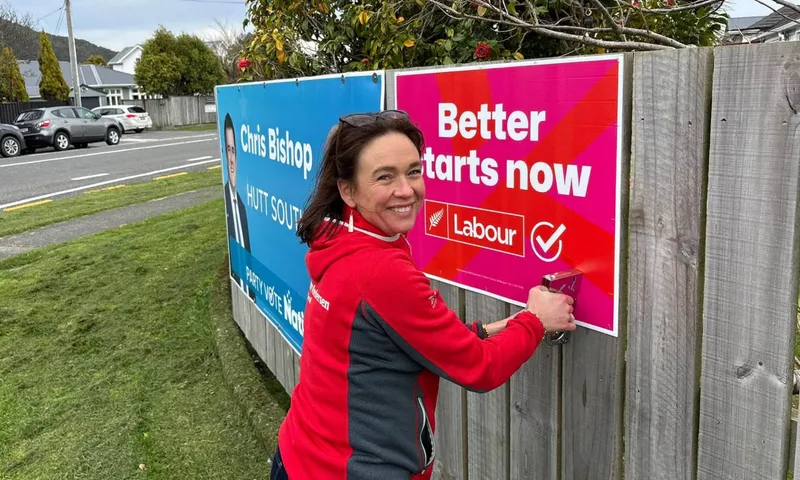 A woman in red grins as she staples a hoarding reading "Better Starts Now" to a wooden fence.