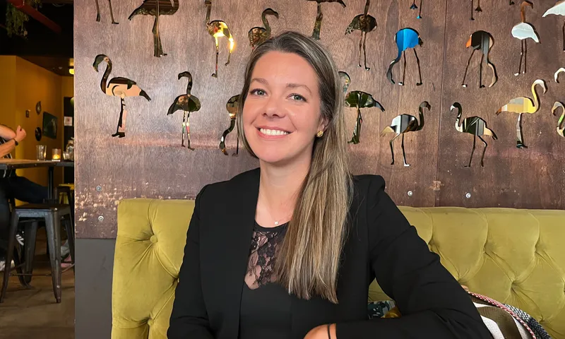 A white woman with blonde highlights grins while sitting on a velvet green couch.