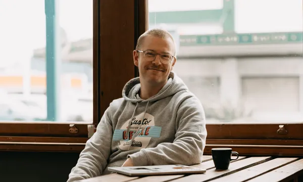 Luke J Barnett, the owner of Sublime Coffee, sits in a grey hoodie and smiles at the camera