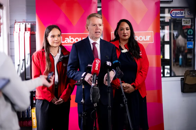 Arena Williams, a brown-haired NZ politician, stands in a red jacket next to Chris Hipkins in a dark suit and Kerrin Leoni in a red coat.