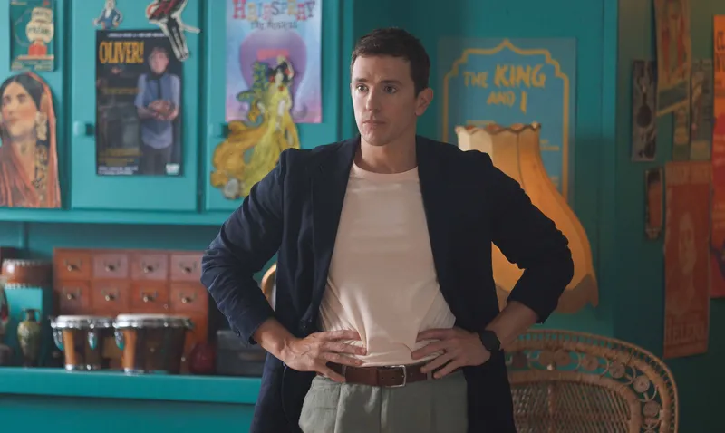 A man wears a black jacket and stands with his arms on his hips in a scene from Happiness