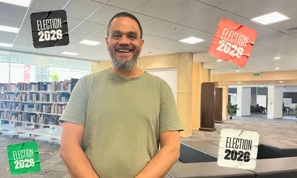 Shalako Rameka smiles for a photograph inside a library, wearing a sage-green T-shirt, with bookshelves behind him and four colourful Election 2026 graphics framing the image.